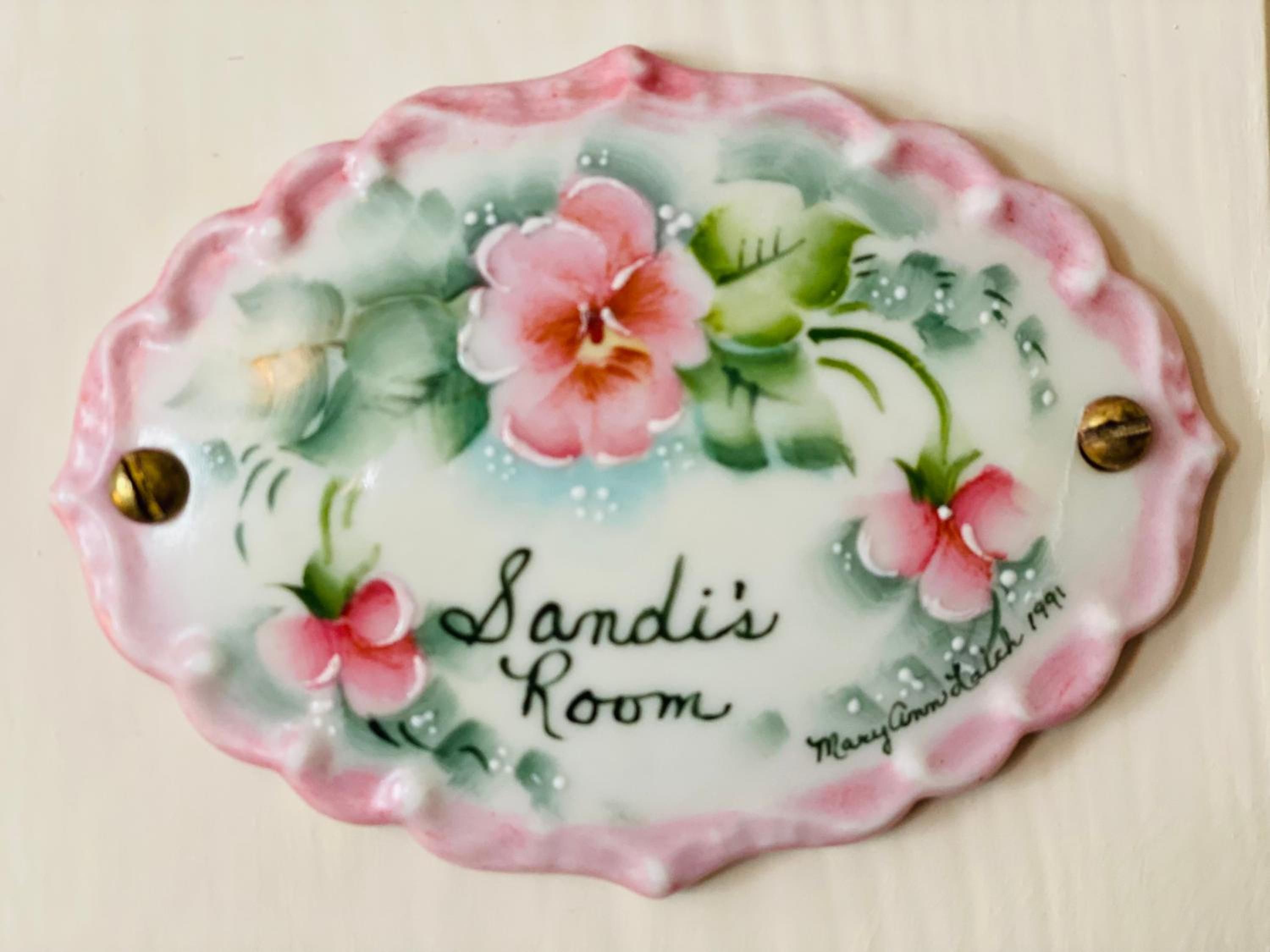 En dekorativ tallerken med blomstermønstre og teksten 'Sandi's Room' samt en webadresse.
