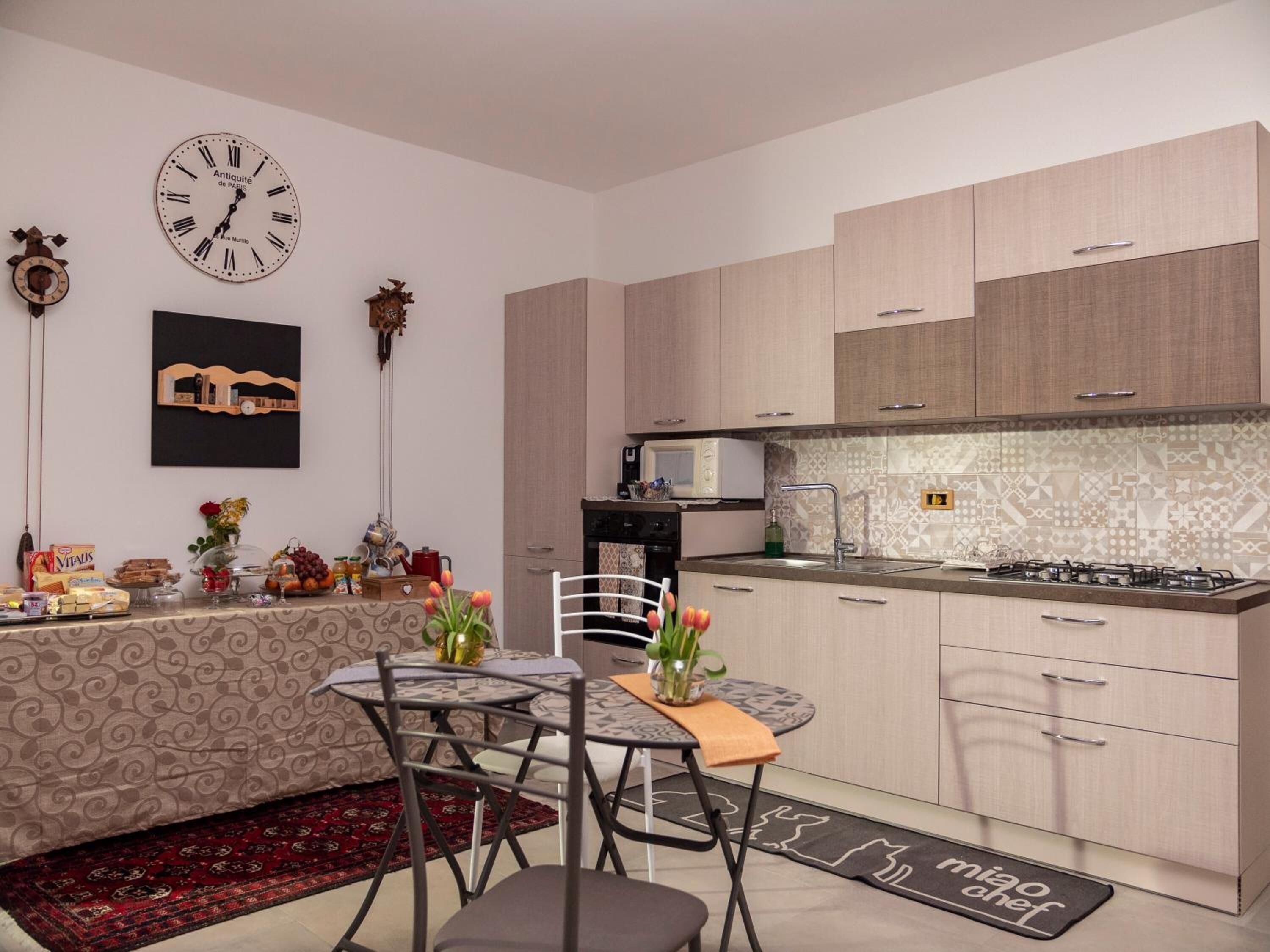 A modern kitchen with light wood cabinets, a gas stove, a microwave, and a decorative clock.