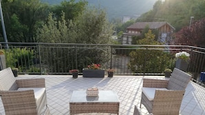 A balcony with wicker furniture and potted plants, overlooking a mountainous area. - La Casa delle Stagioni (L'Aquila)