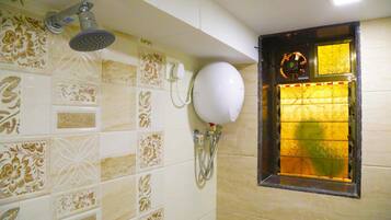 A bathroom with patterned tiles, a handheld showerhead, a wall-mounted toilet paper holder, and a window with a decorative grille.