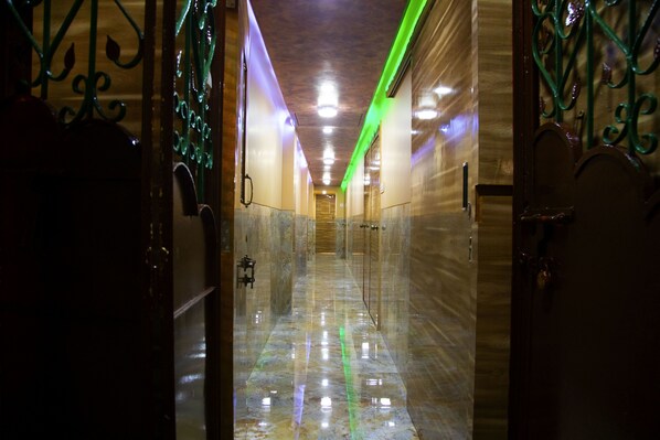 Un pasillo con suelo de mármol reflectante, barandillas decorativas verdes e iluminación empotrada en el techo.