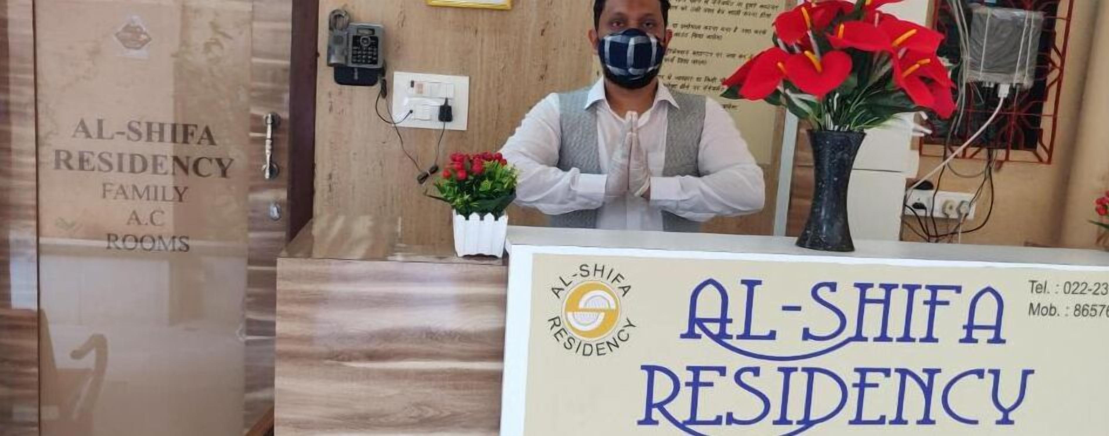 Mostrador de recepción en Al-Shifa Residency con un cartel que muestra el nombre y la información de contacto.