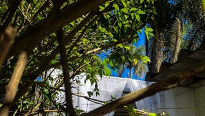 A secluded outdoor seating area with a white canopy and cushions, surrounded by lush greenery and trees.