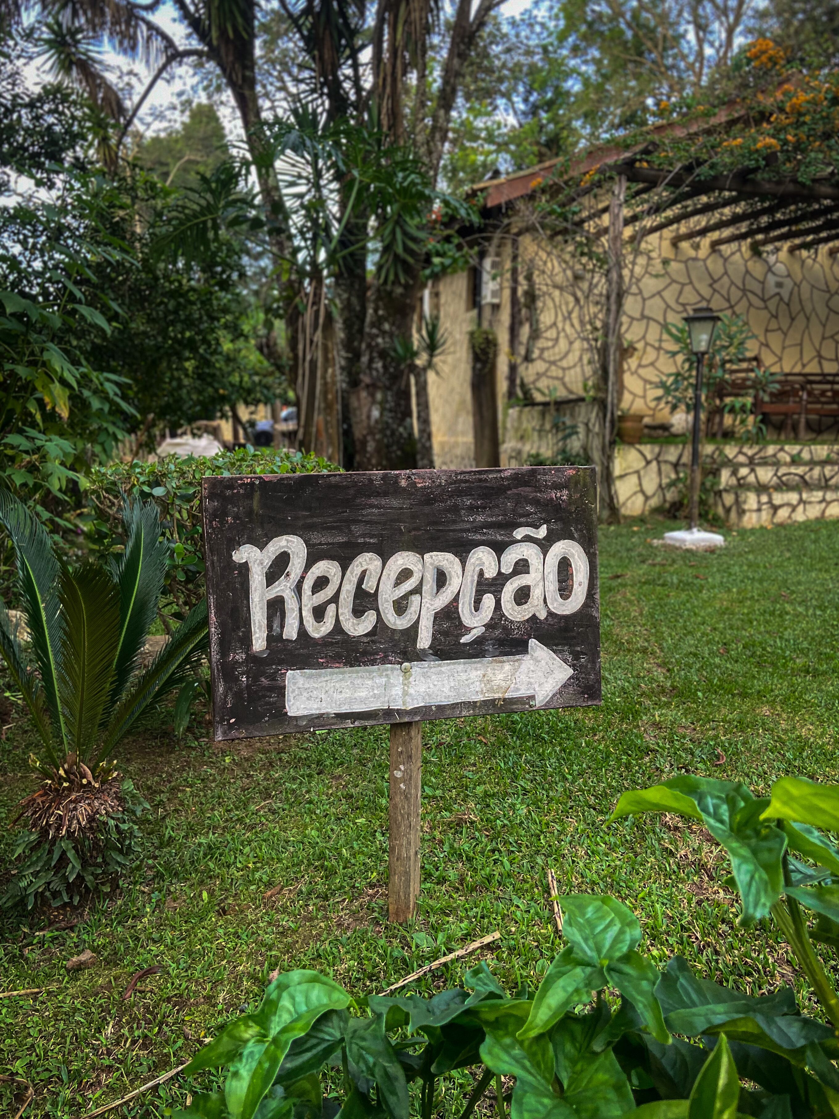 A wooden sign with the word "Recepção" and an arrow pointing to the right, indicating the reception area.