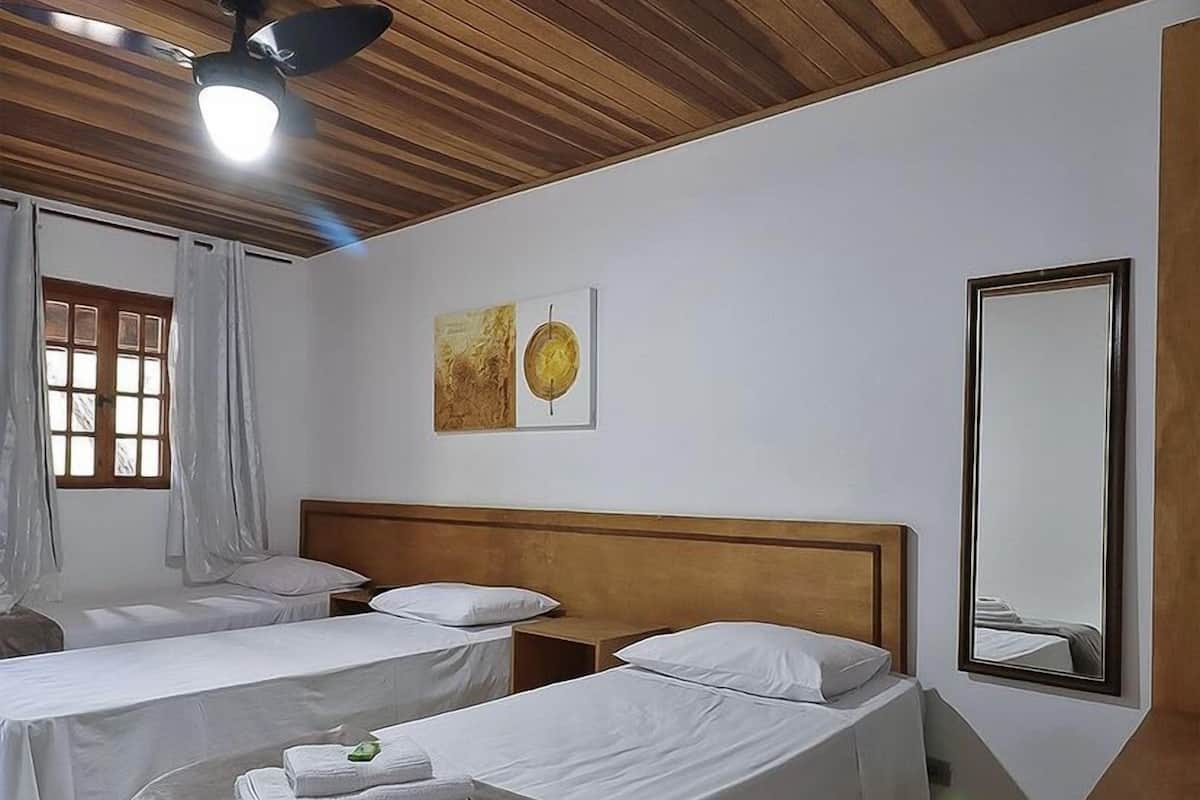 Habitación de hotel con dos camas individuales, ventilador de techo, espejo grande y ventana con cortinas.
