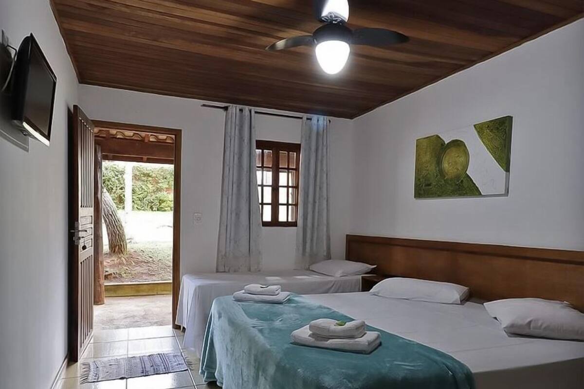 Habitación de hotel con dos camas, ventilador de techo, ventana con cortinas y puerta que da al exterior.