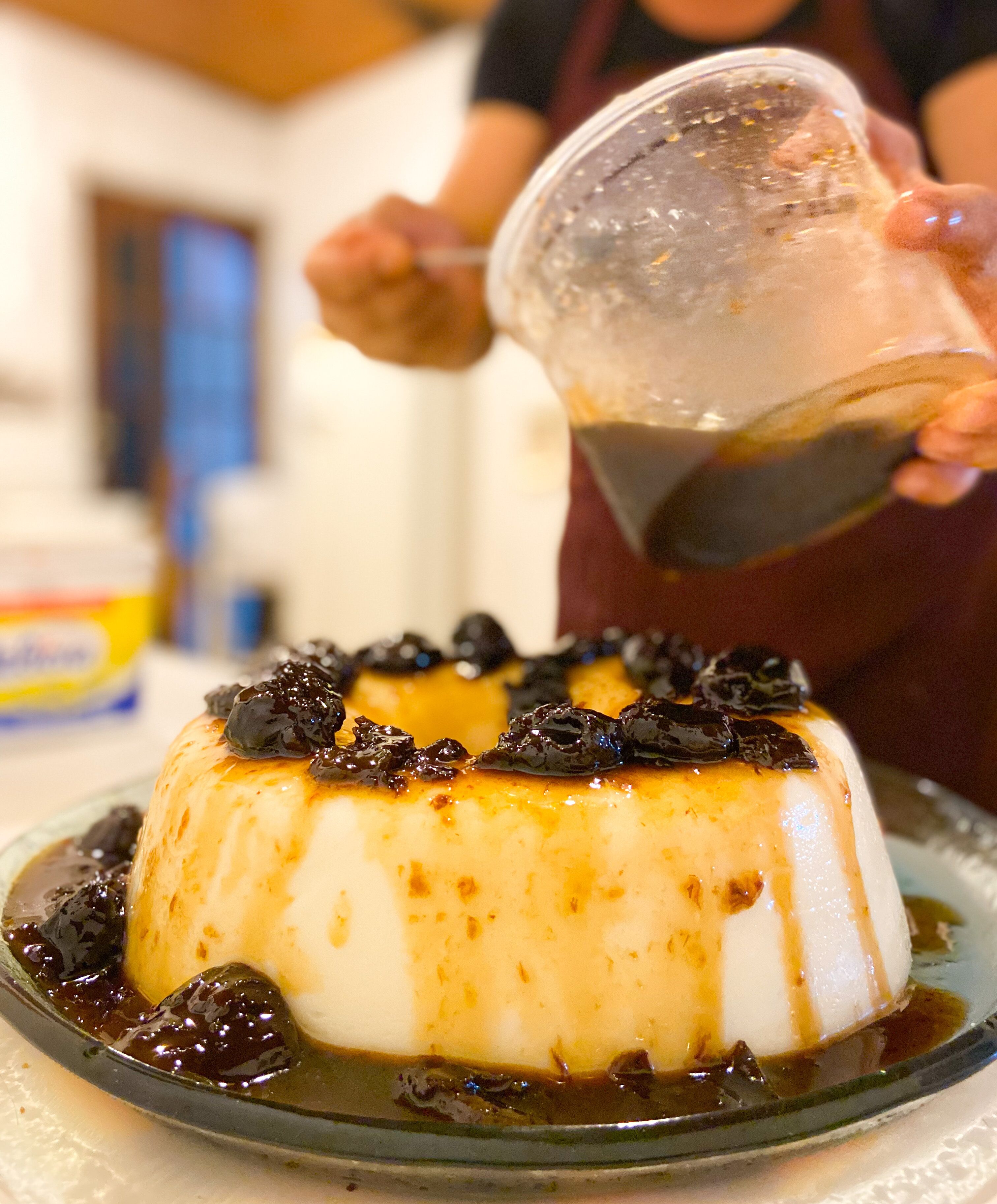 A dessert on a plate with a syrupy topping and a person pouring syrup over it.