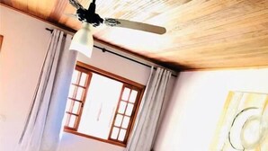 A hotel room with two beds, a ceiling fan, a window with curtains, and a wall with a decorative piece.