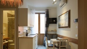 Een compacte keuken met een spoelbak, een klein eetgedeelte met een tafel en stoelen, en een aan de muur bevestigde televisie.