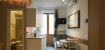 Cocina compacta con un lavamanos, un pequeño comedor con mesa y sillas, y un televisor montado en la pared.