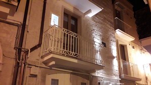 Een gebouw met meerdere balkons, waarvan sommige metalen hekken en andere witte hekken hebben. Op de buitenmuren zijn leidingen en elektrische buizen zichtbaar.