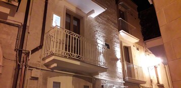 Un edificio con varios balcones, algunos con barandillas metálicas y otros con barandillas blancas. Se observan tuberías y conductos eléctricos en las paredes exteriores.