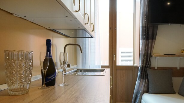 Een kleine keuken met een roestvrijstalen spoelbak, een wijnglas en een fles wijn.