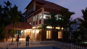 A multi-story hotel with a red roof and white walls, surrounded by palm trees and a white picket fence. - Kimberly By Jade (Kunigal)