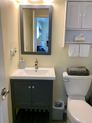 Une salle de bain avec un lavabo blanc, un miroir, des toilettes et une petite poubelle.