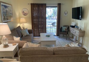 Una sala de estar con un sofá, una mesa de centro, una lámpara, un televisor y vistas al exterior por una ventana.