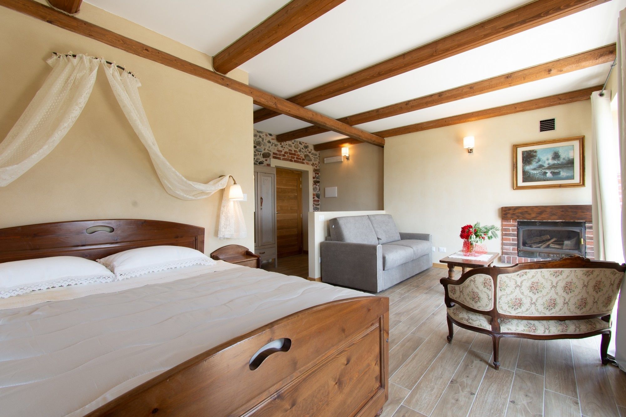 Una camera da letto con un letto di legno, un divano grigio, una poltrona con motivi floreali e un camino.