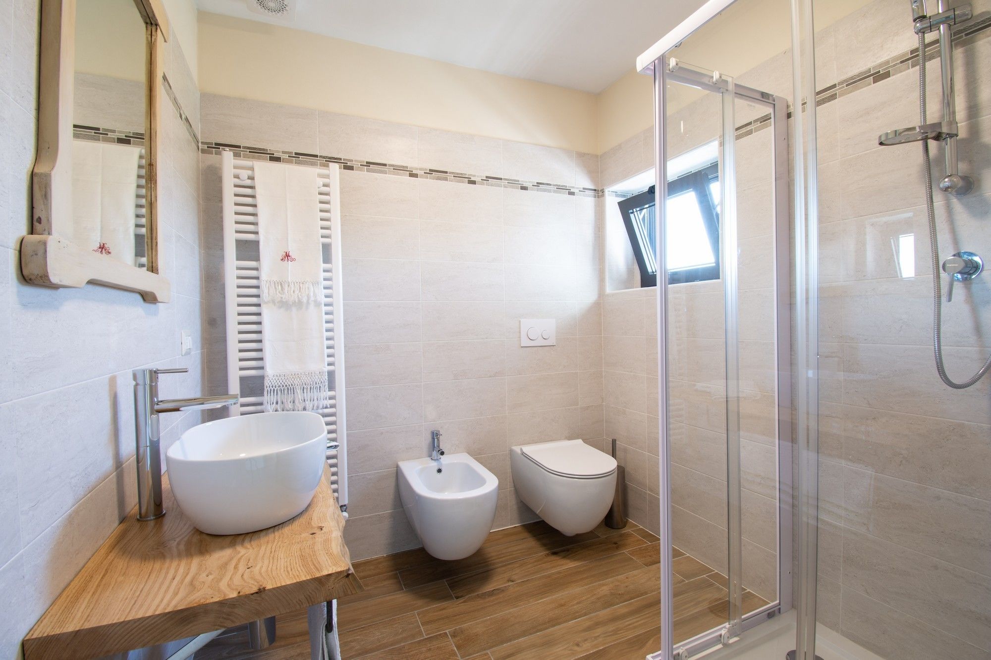 A modern bathroom with a large white sink, a bidet, a toilet, and a glass-enclosed shower area.