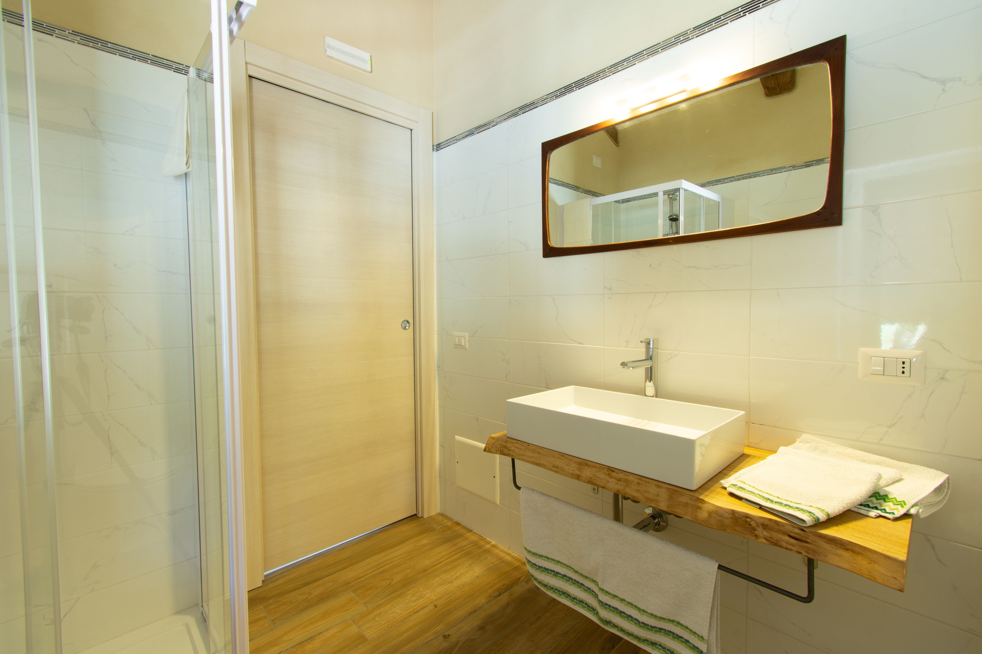 A bathroom with a wooden vanity, a white sink, a mirror, and a shower enclosure.