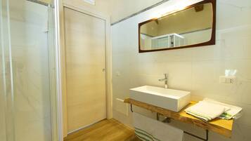 A bathroom with a wooden vanity, a white sink, a mirror, and a shower enclosure.