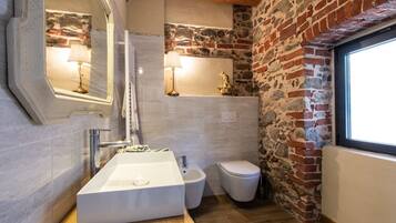 Ein Badezimmer mit einem großen weißen Waschbecken, einem Bidet, einer Toilette und einer Steinwand.