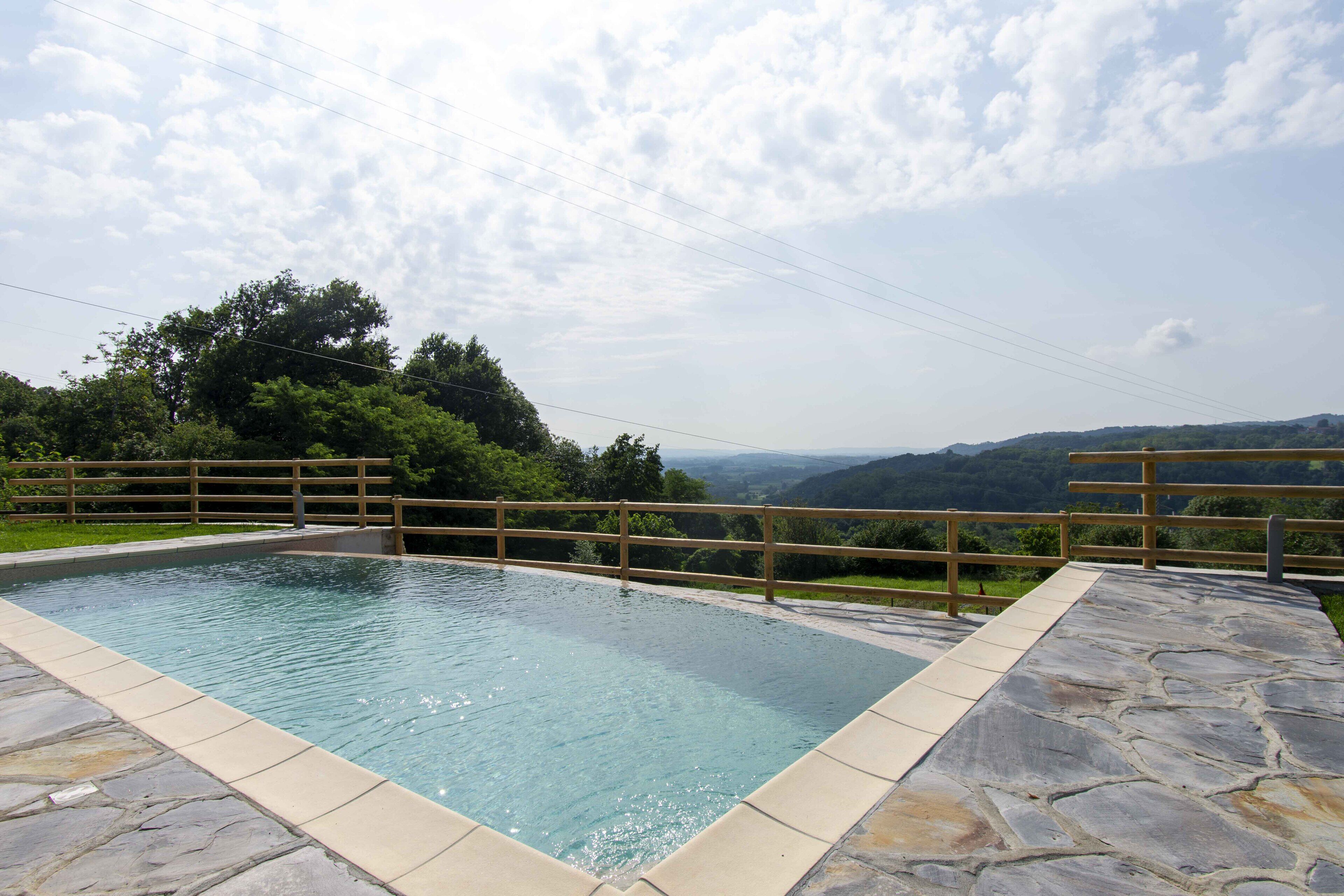 Ein rechteckiger Swimmingpool mit Steinrand, umgeben von einer Holzterrasse und einem Holenzaun.