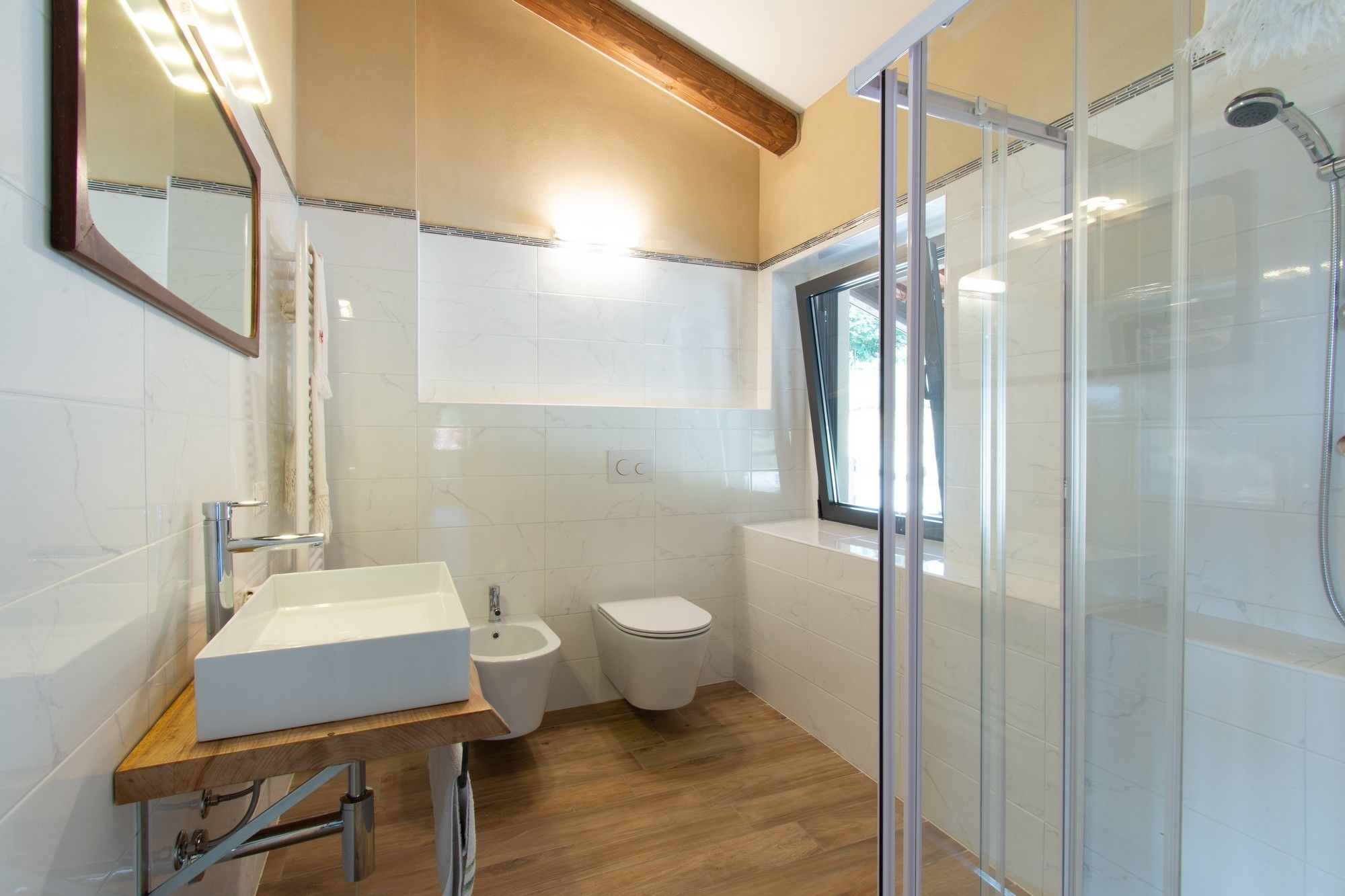 Et moderne badeværelse med en trækommode, en hvid vask, et toilet, en bruser med glasvægge og et bidet.