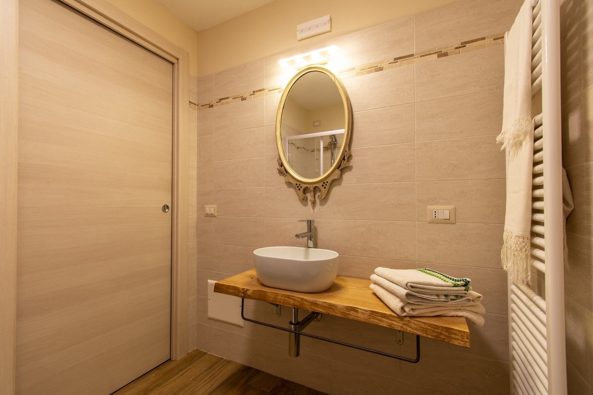 Un baño con un lavamanos blanco, un tocador de madera, un espejo con un marco ornamentado y un perchero con toallas dobladas.