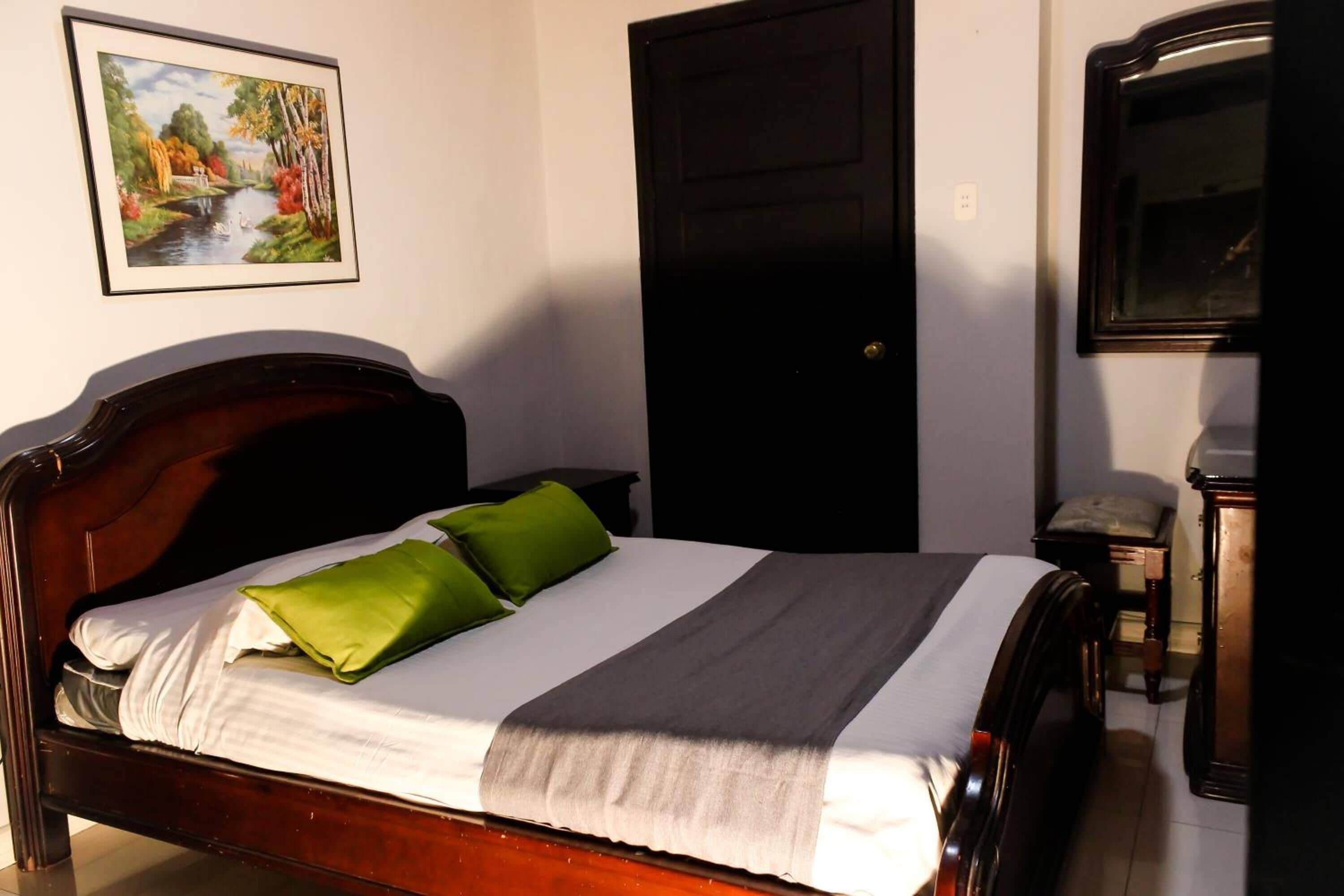 Un lit bien fait, avec une tête de lit en bois, un oreiller vert et une couverture grise.