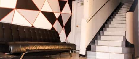 A modern interior with a black leather sofa, a geometric patterned wall, and a staircase.