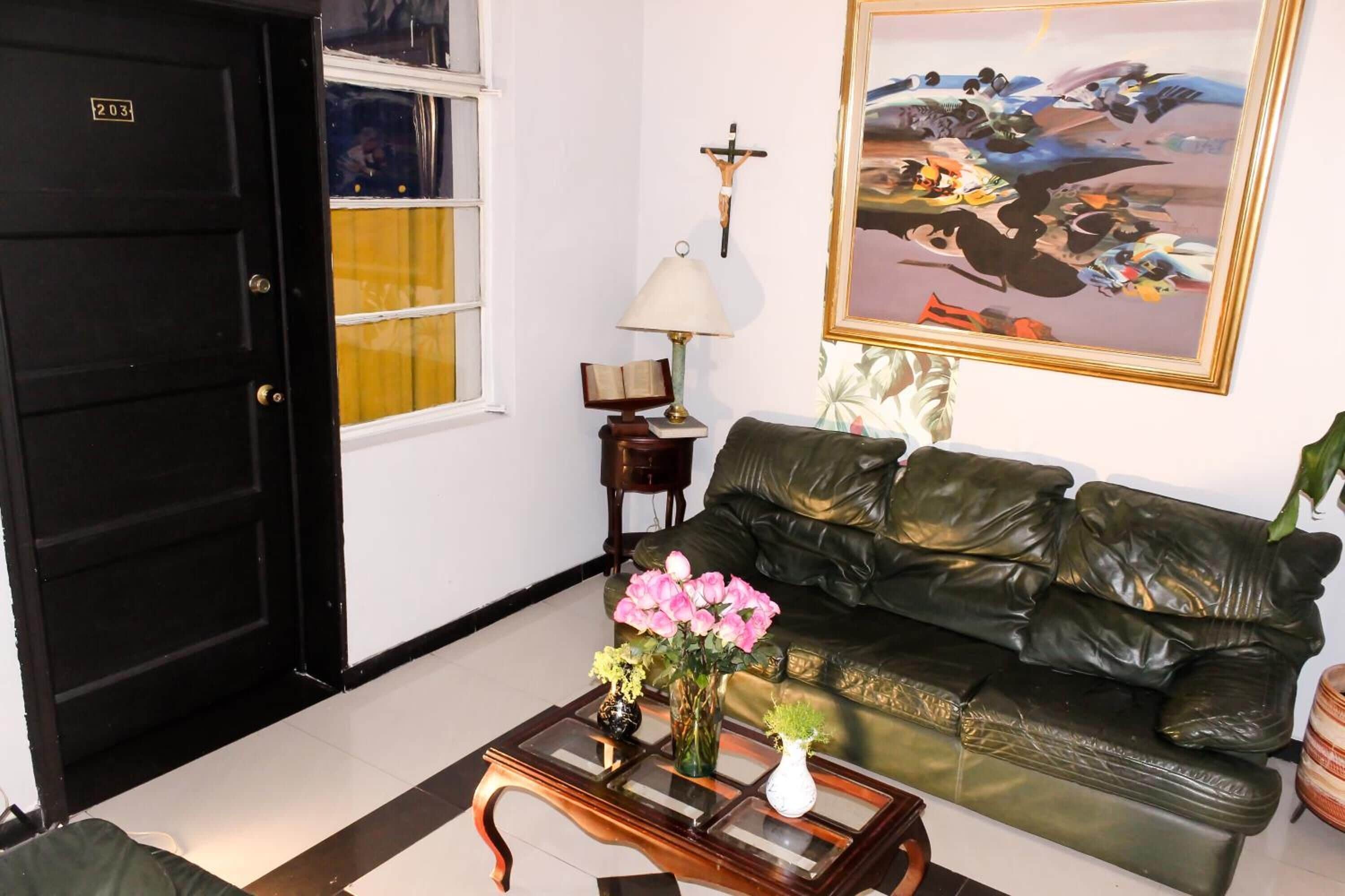 Un salon avec une porte noire, un canapé vert, une table basse ornée de vases, une lampe et un tableau accroché au mur.