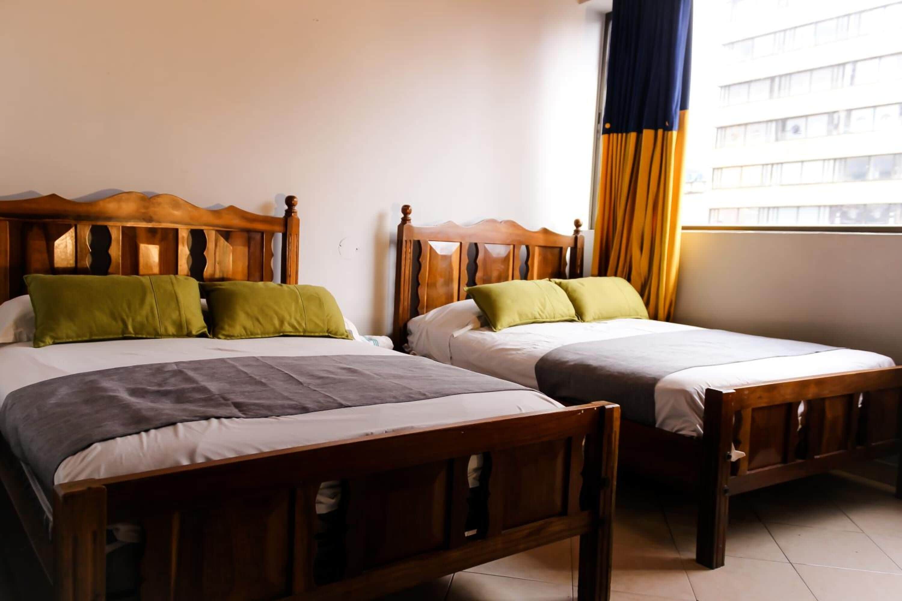 Two wooden beds with headboards, a window with curtains, and a tiled floor.