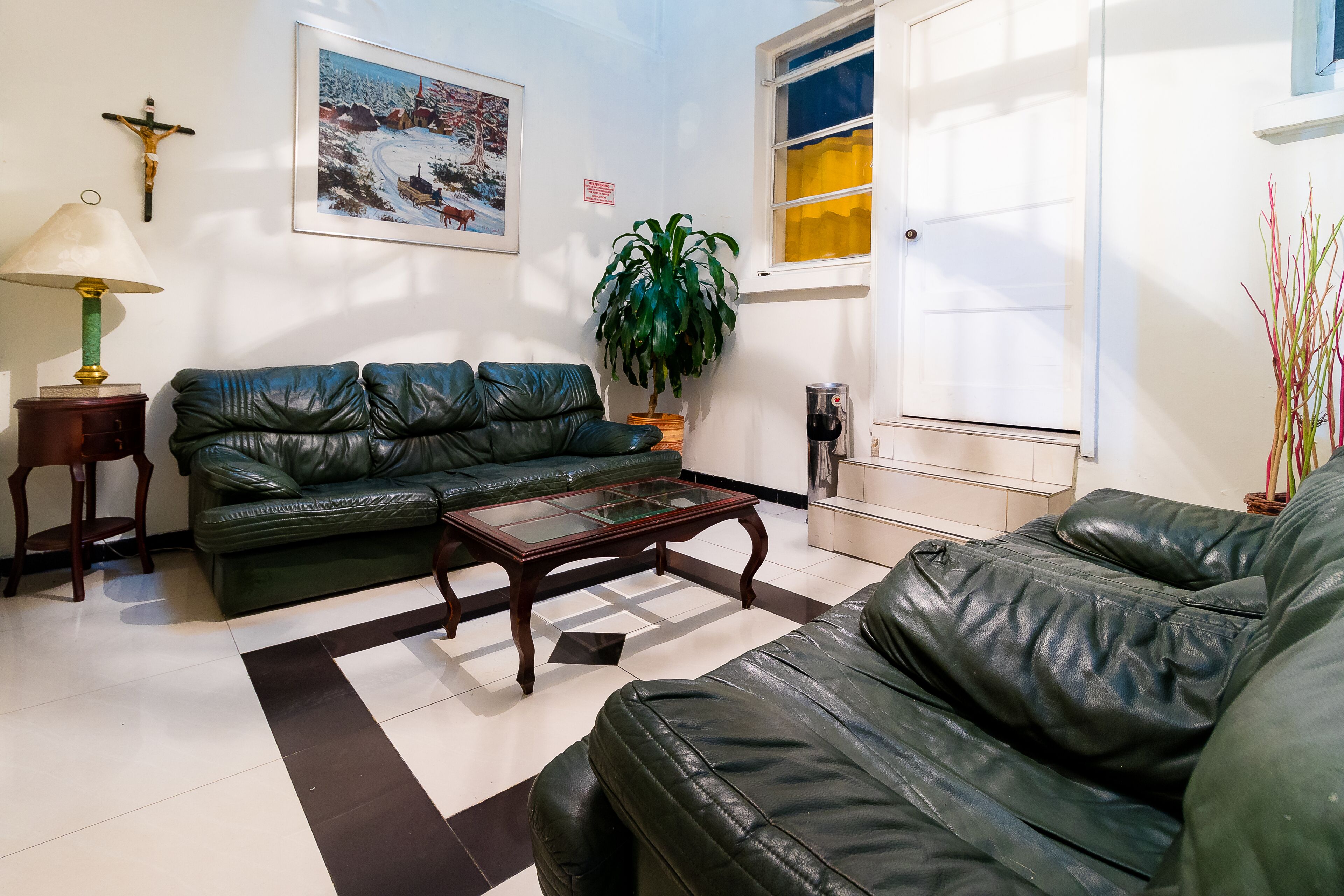 A living room with a green leather sofa, a wooden coffee table, a potted plant, a crucifix, and a framed picture on the wall.