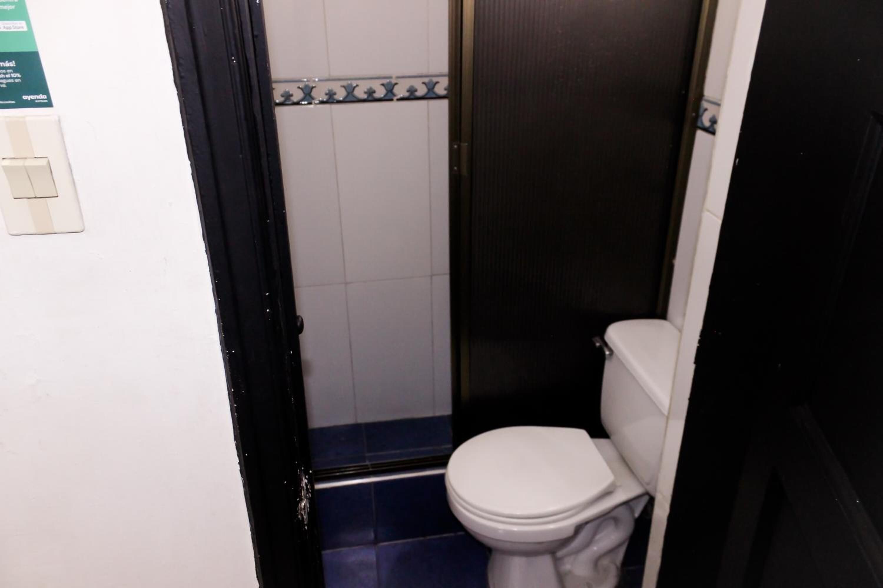 A small, narrow bathroom with a white toilet, a shower area, and a tiled floor.