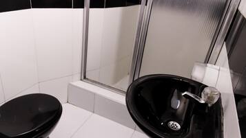 A bathroom with a black toilet, a black sink, and a glass shower enclosure.