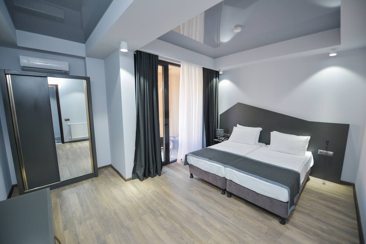 A modern hotel room with a large bed, a wardrobe, and a sliding door leading to a balcony.