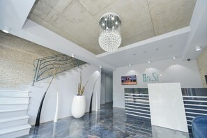 Um hall moderno de hotel, com uma mesa de recepção, escadaria e um lustre.