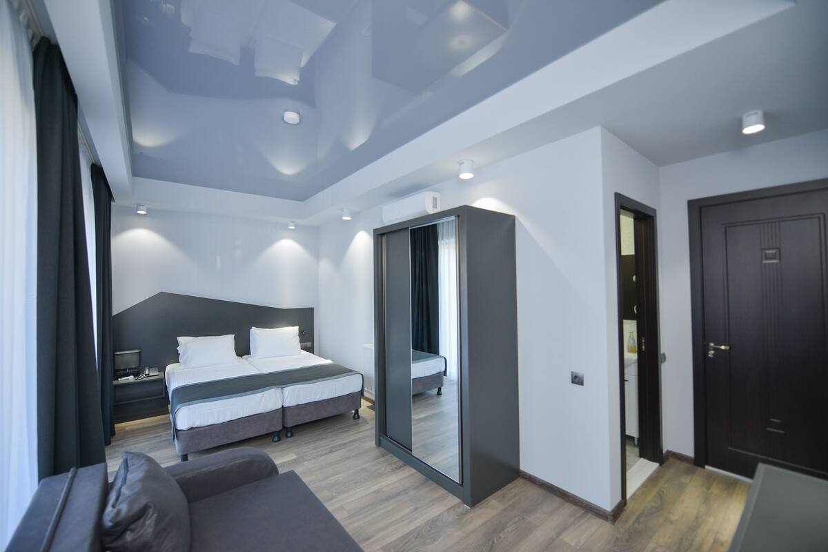 A modern hotel room with a large bed, a sofa, a mirror, and a wardrobe.