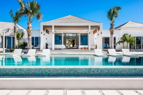 Un resort moderno con piscina cristalina, sillas de descanso y palmeras.