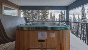 Un jacuzzi de madera en un balcón con vistas a árboles cubiertos de nieve.