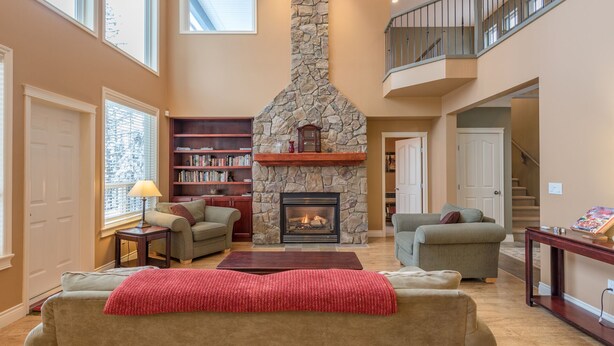Un salón espacioso con chimenea de piedra, dos sofás, una estantería y una escalera que sube a un nivel superior.