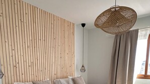 Une chambre moderne avec deux lits, un mur en lambris de bois, un luminaire suspendu en fibres tressées et une vue sur l’extérieur.