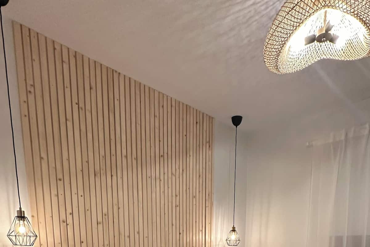 Een moderne slaapkamer met een wand van houten latten, een bed met een bruine plaid en twee hanglampen.