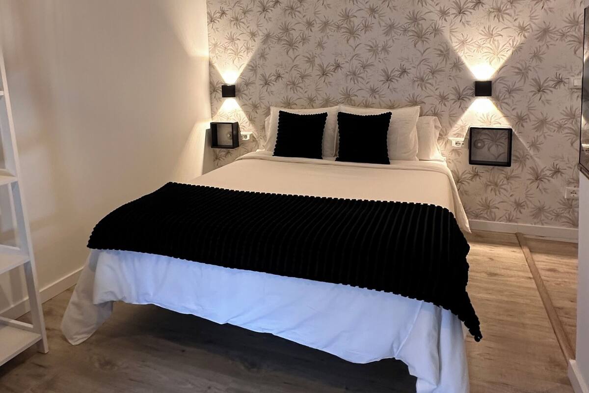Een slaapkamer met een bed, twee bedlampen, behang met een patroon en een houten vloer.