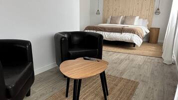 Un dormitorio moderno con cama, un sillón de cuero negro, una mesita de madera y una alfombra tejida.