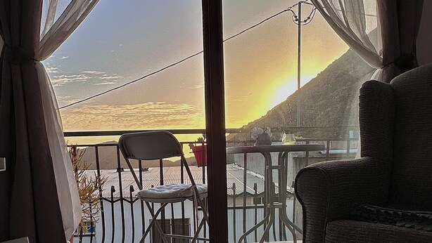 Une pièce avec vue sur le coucher de soleil au-dessus d’une étendue d’eau, comprenant une chaise et un canapé.