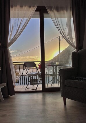 Une pièce avec vue sur le coucher de soleil au-dessus d’une étendue d’eau, comprenant une chaise et un canapé.