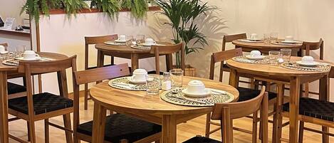 Un comedor con mesas y sillas de madera, una lámpara decorativa colgante y plantas en macetas.