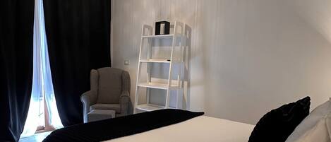 A modern bedroom with a large bed, a white wardrobe, a chair, and a hanging light fixture.