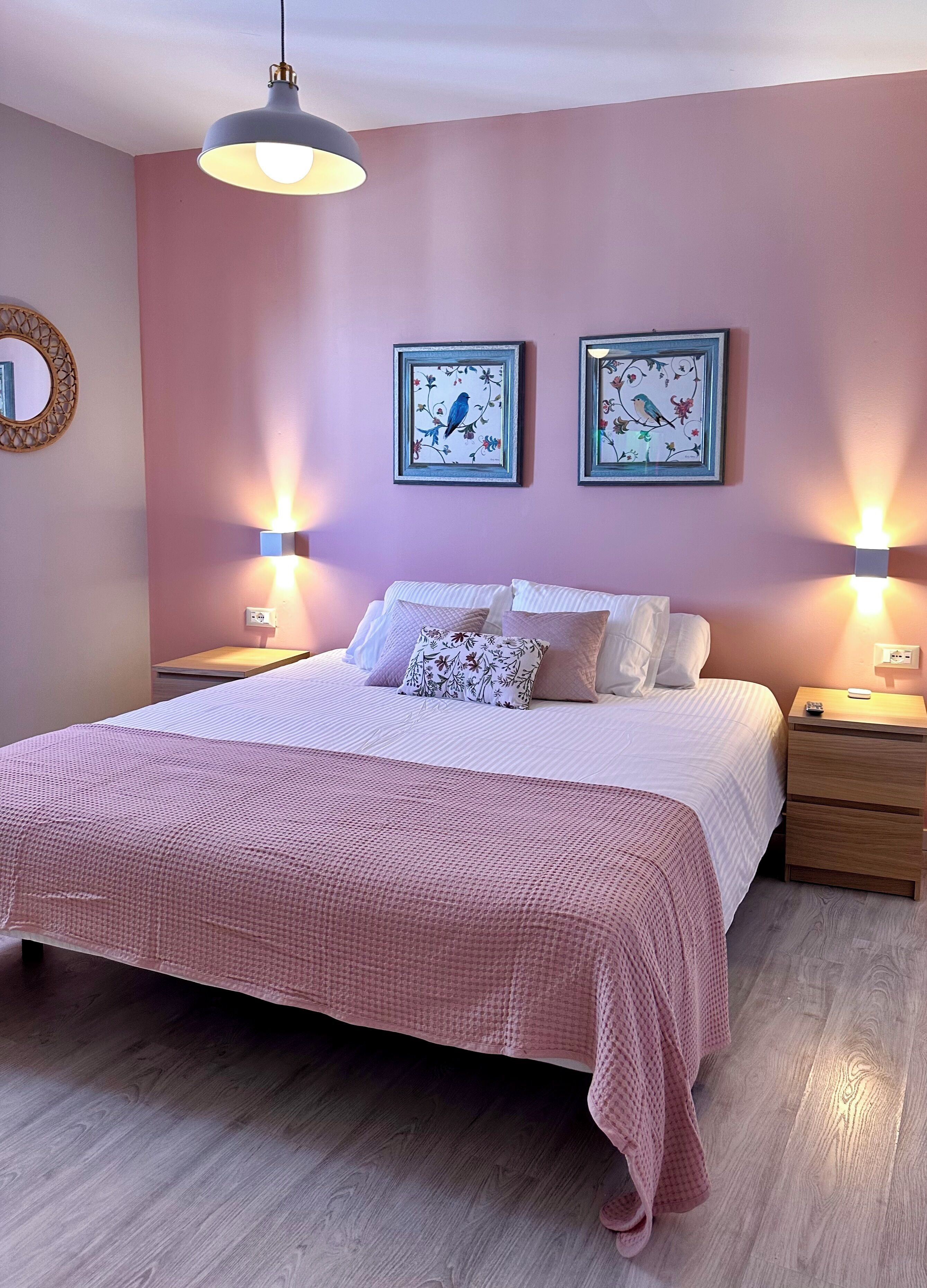 Un dormitorio con una cama grande, dos cuadros colgados en la pared, lámparas de noche, una mesita de noche de madera y un espejo.